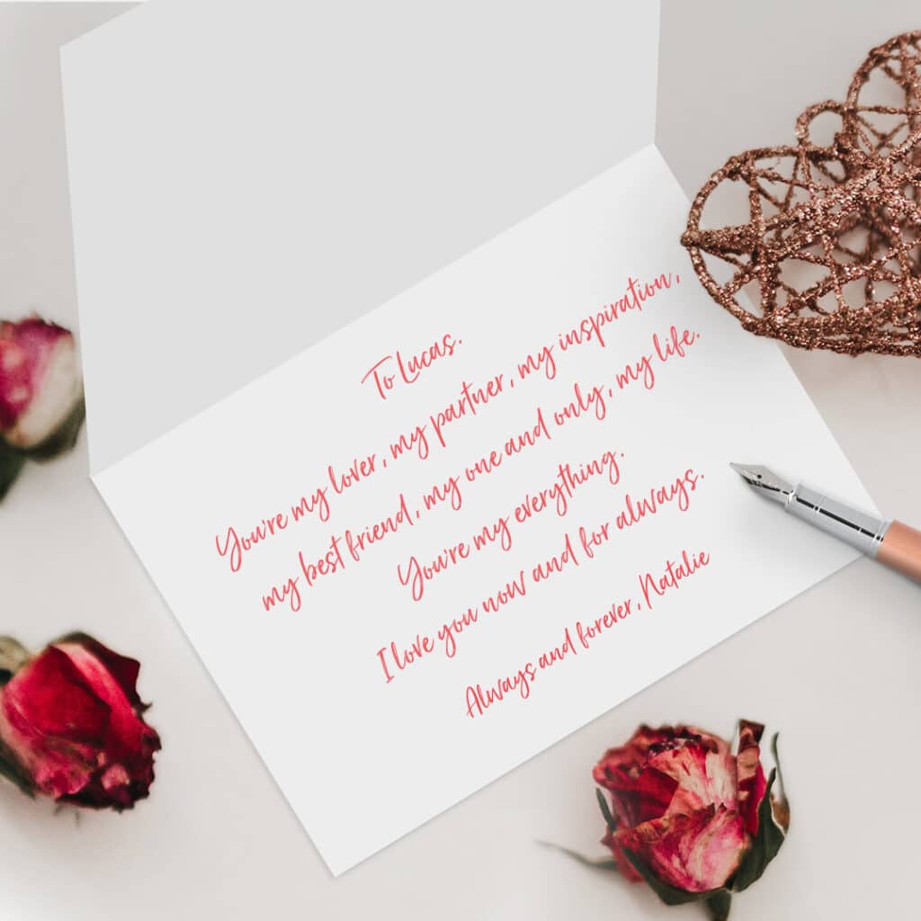 Card with handwritten message lying open on a table with pen and flower buds