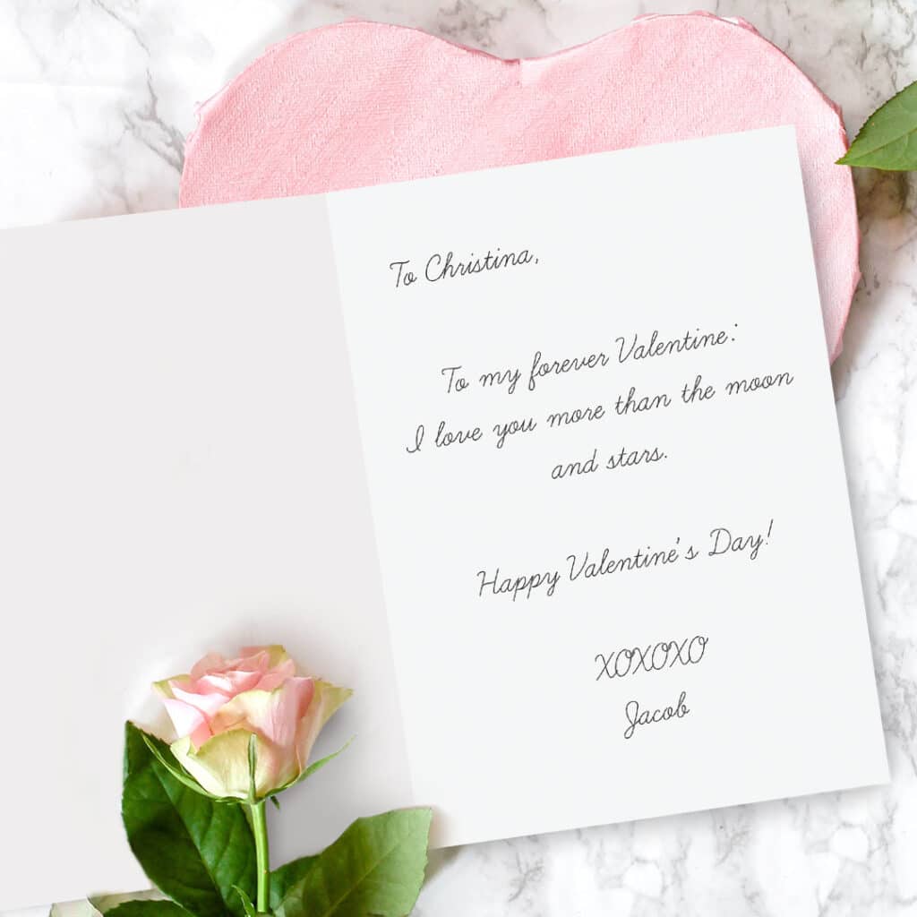 Card with handwritten message lying open on a table with rose
