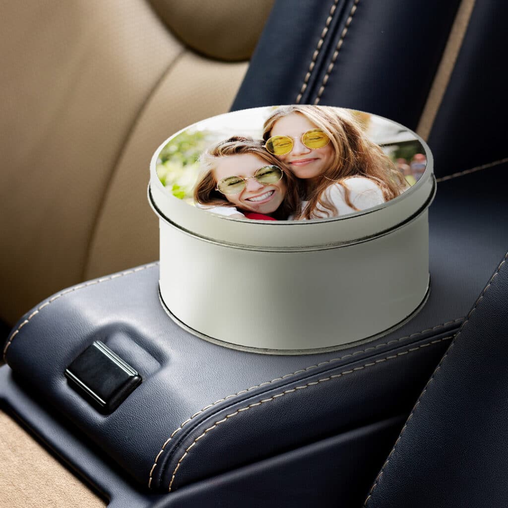 A personalised round tin with an image of 2 friends on the lid, placed inside a car