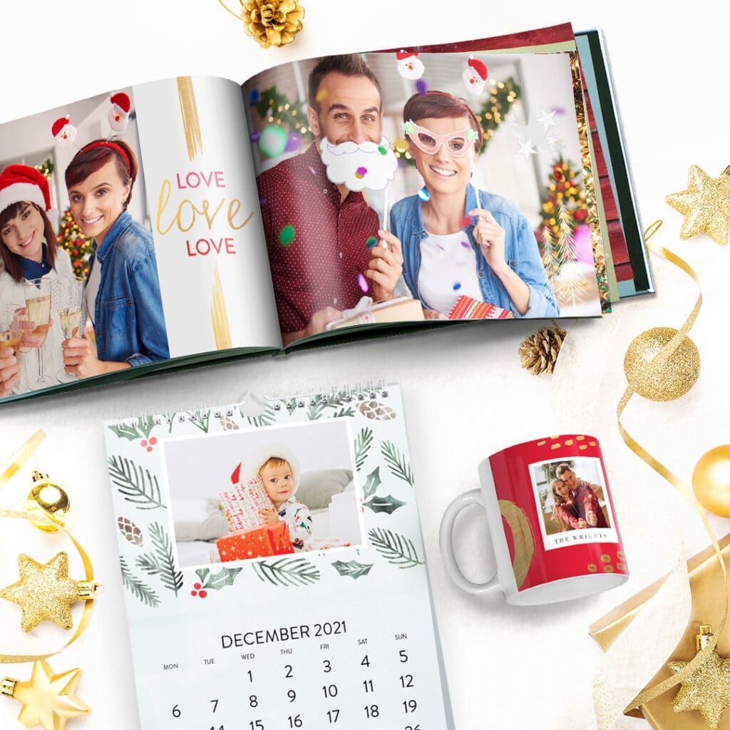 a Christmas photo book, calendar and a mug presented on a surface with golden baubles and stars