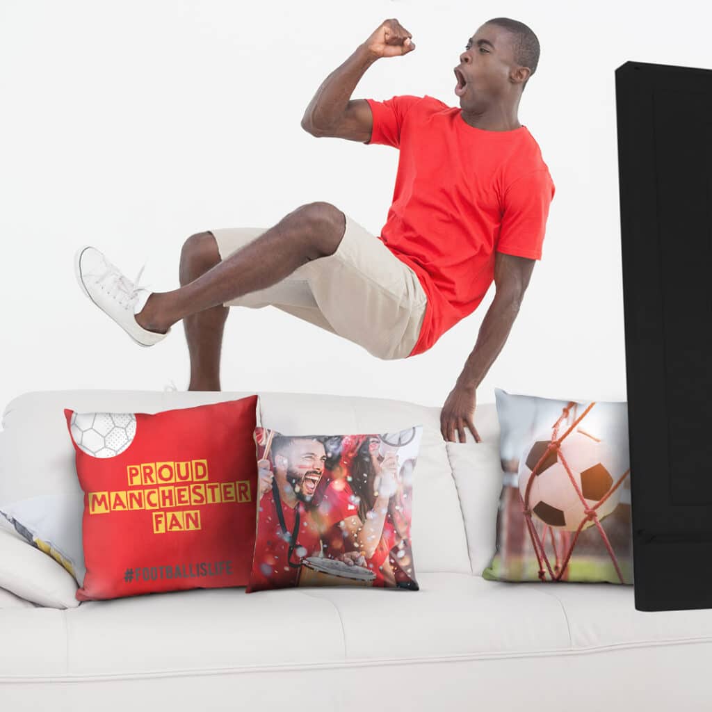 a Manchester fan jumping next to a couch full of football fan cushions