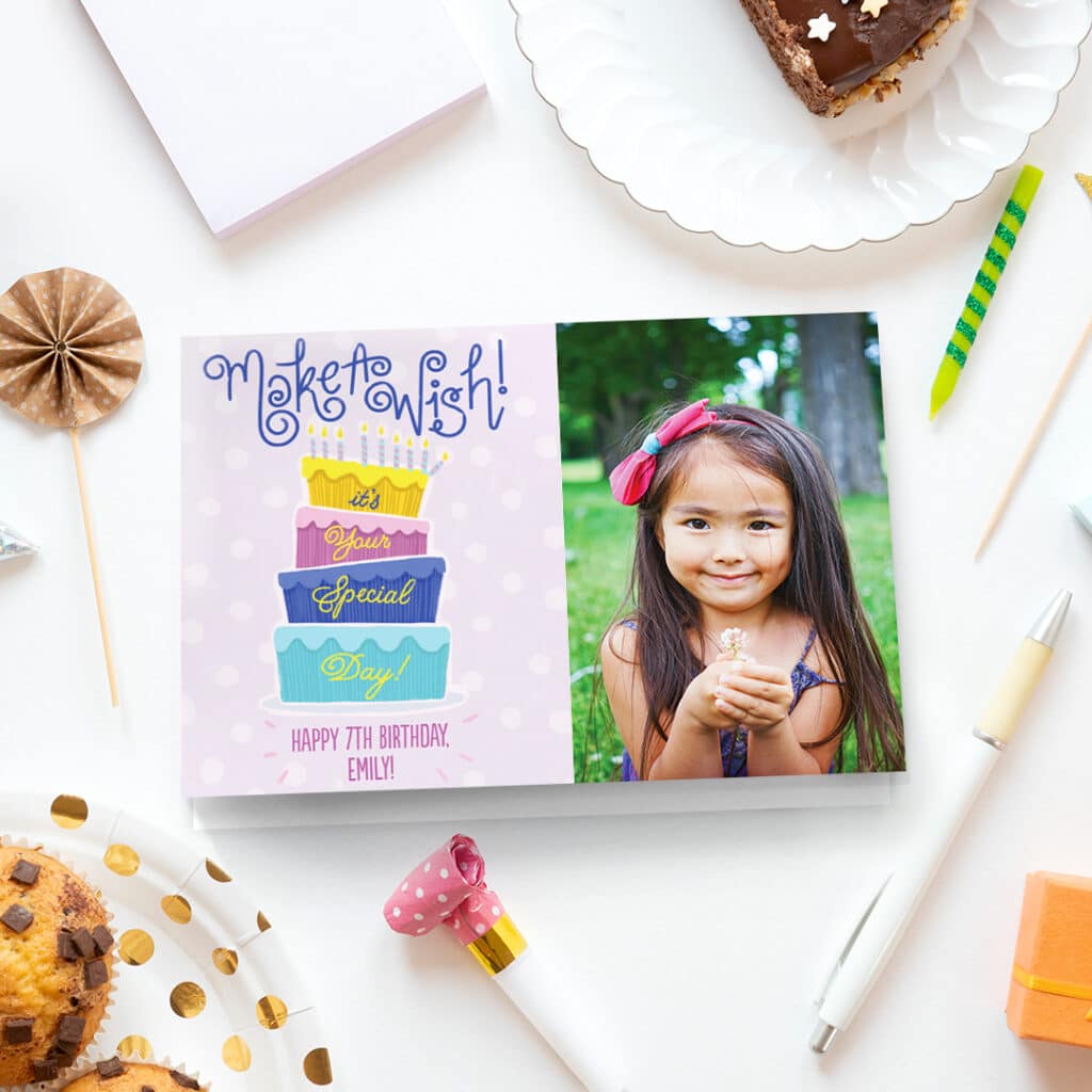 A lovely pink happy birthday card presented on a table next to birthday candles and a piece of cake