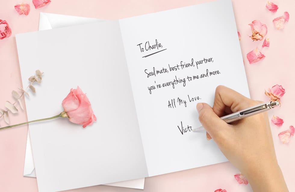 Open card with a hand writing a love message inside with a pen